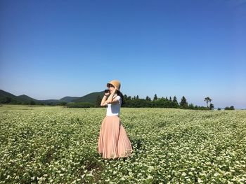 Young woman standing on field against clear sky