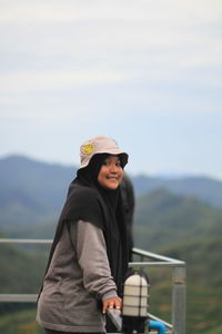 Portrait of woman standing by railing against sky