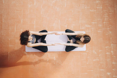 Directly above shot of female friends doing yoga while sitting on coral colored flooring