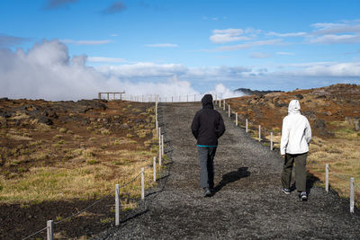 Rear view of tourists walking towards gunnuhver hot springs at reykjanes peninsula, iceland