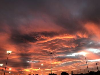 Low angle view of illuminated street lights against dramatic sky