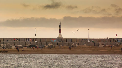 Group of people on industry against sky at sunset