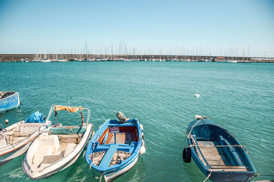 Sailboats moored in sea against clear blue sky