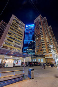 Illuminated buildings by street against sky at night