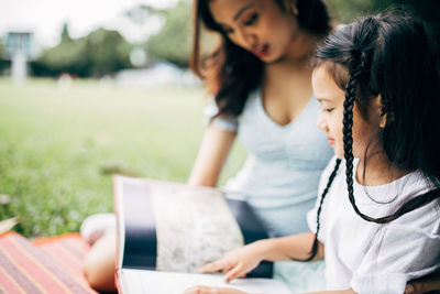 Smiling teacher and girl reading book sitting at park