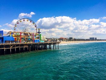 View of ferris wheel in sea against cloudy sky