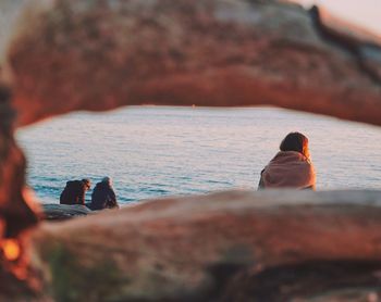 Rear view of women sitting on rock by sea