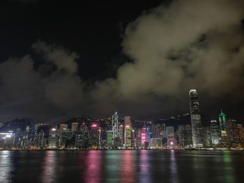 Illuminated city by river against sky at night