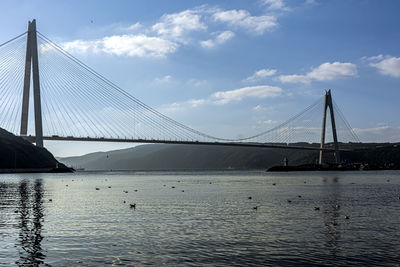 View of suspension bridge over river against cloudy sky