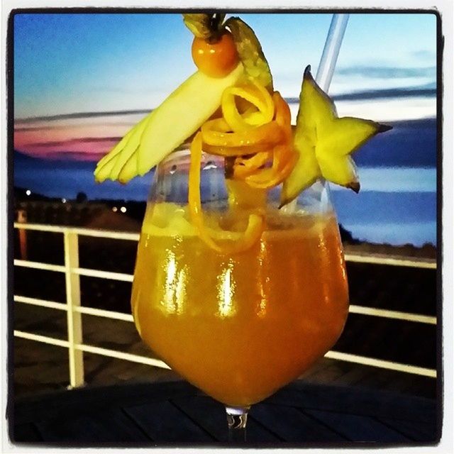 yellow, sky, transfer print, drink, close-up, blue, focus on foreground, alcohol, auto post production filter, food and drink, glass - material, illuminated, drinking straw, orange color, transparent, refreshment, sunset, outdoors, lighting equipment, cocktail