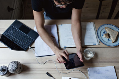 High angle view of studious young man using digital tablet while doing homework at table