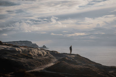 Man standing on rock by sea against sky