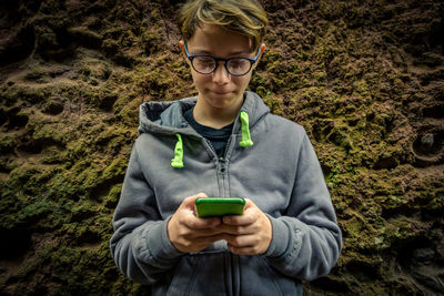 Smiling boy using mobile phone against rock