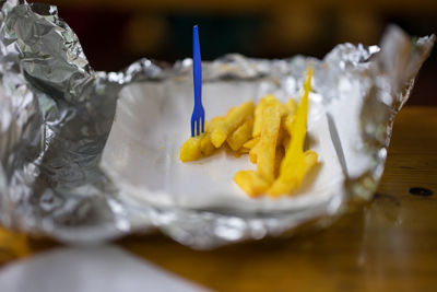 High angle view of french fries on foil with plastic fork on table