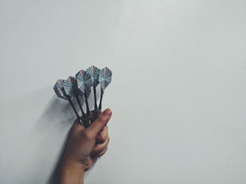 Close-up of hand holding darts against white background