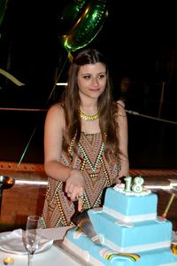 Smiling young woman cutting birthday cake while standing at table