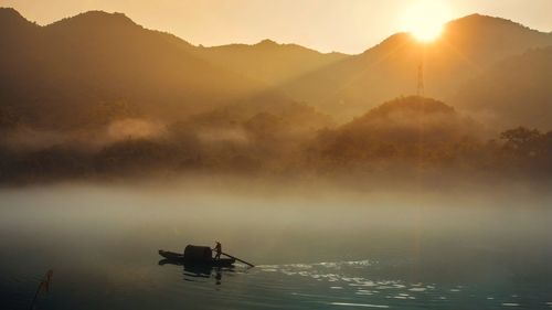 Silhouette man on boat in lake against mountains during sunset