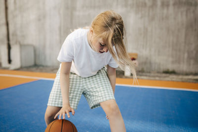 Blond girl practicing basketball at court