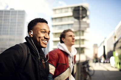 Teenage boys resting at roadside against buildings in city on sunny day