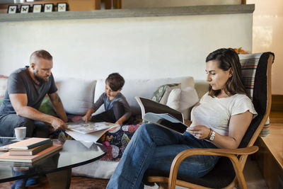 Woman reading magazine while father and son studying in background at home