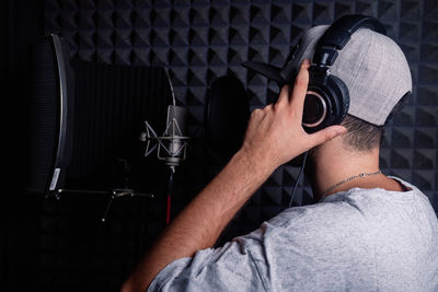 Side view of anonymous male singer in headphones standing in acoustic room with soundproof walls and microphone and recording song in studio