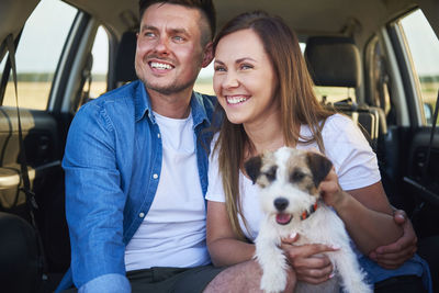 Smiling couple with dog sitting in car