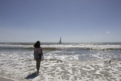 Rear view of man walking on beach against clear sky