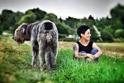 Smiling woman with irish wolfhound sitting on grassy field