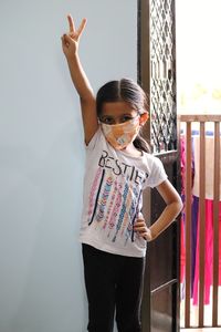 Full length portrait of girl wearing face mask standing against wall