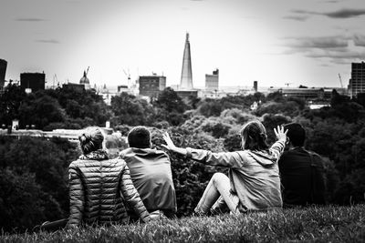 Rear view of friends sitting on grass in park against sky