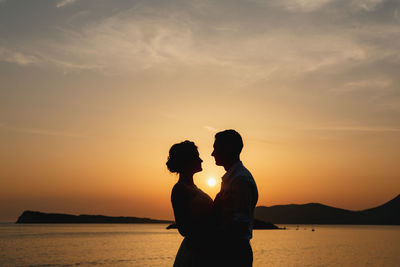 Silhouette couple standing by sea against sky during sunset