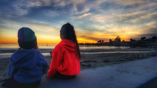 Rear view of people on beach against sky during sunset