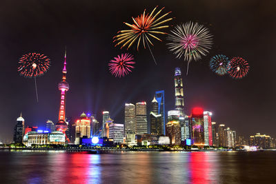 Firework display over river against illuminated buildings in city at night