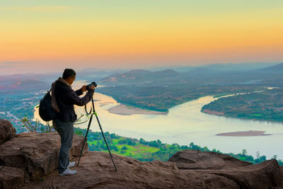 Man photographing on mountain against sky during sunset