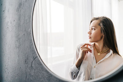 Woman looking away while sitting on window