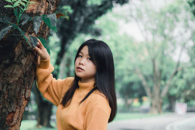 Portrait of beautiful young woman standing by tree trunk