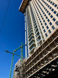 Low angle view of crane by building against clear blue sky