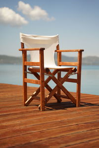 Canvas chair in the sun on a wooden deck with blue ocean and mountains behind