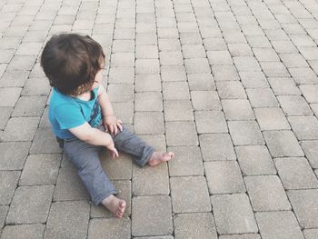 High angle view of boy sitting on cobblestone