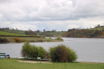 Scenic view of river and green landscape against cloudy sky