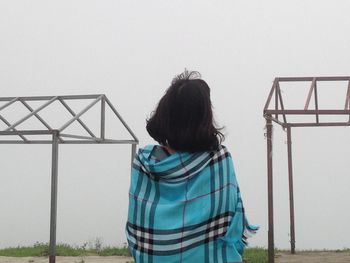 Rear view of woman with blanket standing against clear sky