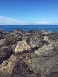 Rocks on sea shore against blue sky