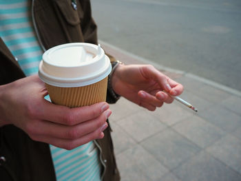Midsection of man holding cigarette on street