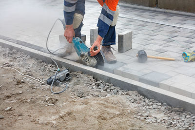 A worker with an electric grinder cuts paving slabs at a construction site.