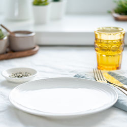 Side view of clean empty white plate, glass of water, fork and knife on white tablecloth on table