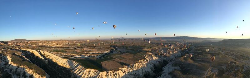 Panoramic view of hot air balloons over landscape against clear blue sky during sunset