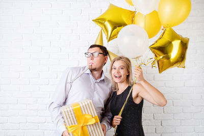 Happy young couple holding balloons against wall