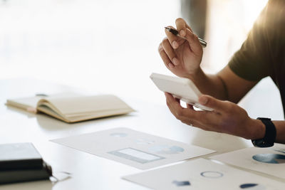 Cropped hands of woman using mobile phone on table
