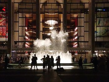 People at illuminated building in city at night