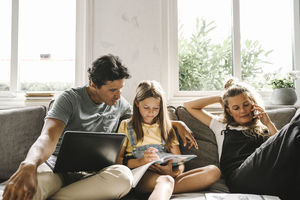 Daughter doing homework sitting by mother and father in living room